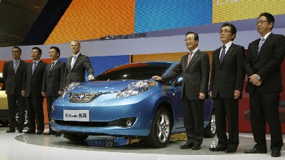 officials pose beside a Venucia e30 electric car created by the joint venture of Dongfeng and Nissan at the company's booth during the Guangzhou Auto Show